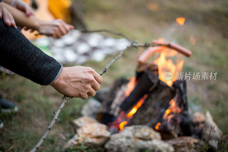 漂亮的一对，围坐在篝火旁。背景是一个帐篷，那人用一根棍子弹火。