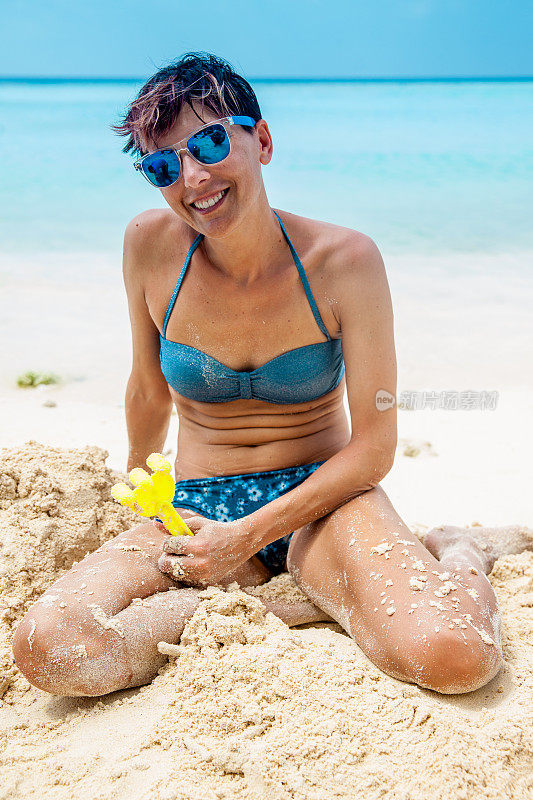 微笑的成年妇女坐在沙滩上玩耍