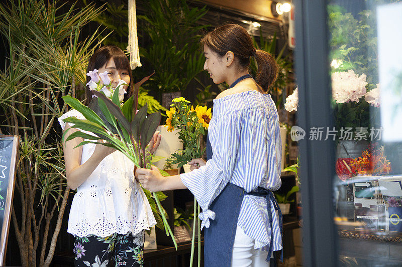 在花店里帮助一位挑选向日葵和树叶的妇女的店员。