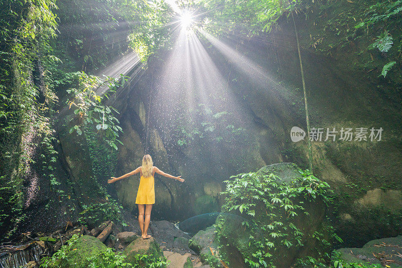 在巴厘岛的热带雨林中，旅行的年轻女子张开双臂拥抱大自然的美丽。人们以自然为旅游理念。