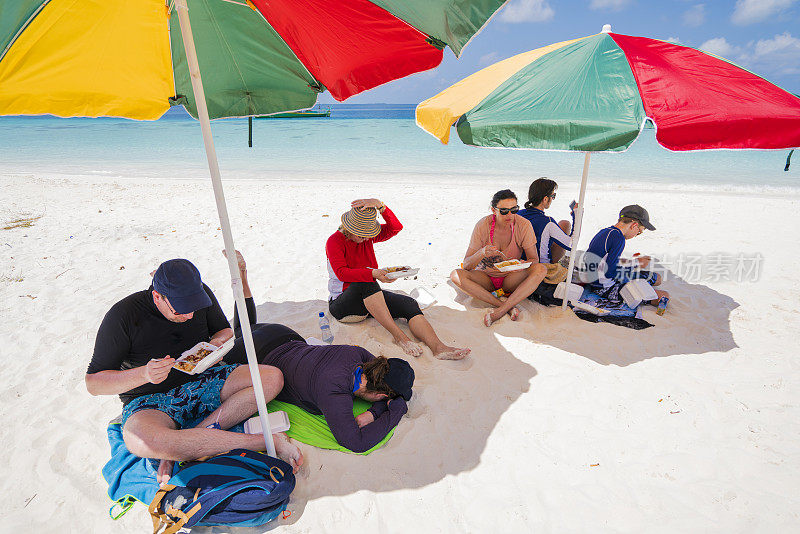 游客在马尔代夫Maffushi岛附近的沙洲上，在五颜六色的保护伞下享用午餐