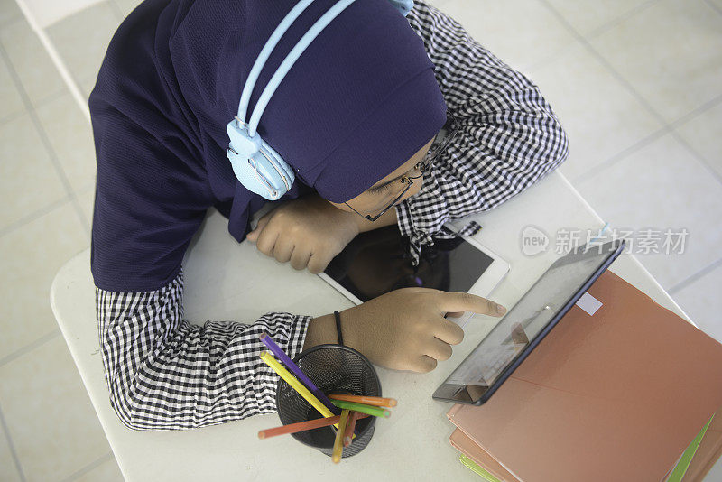 亚洲少女戴着耳机用平板电脑做作业