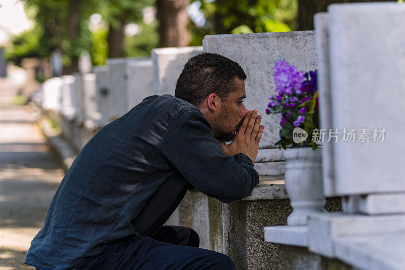 情绪紧张的黑衣男子跪在他家人的墓前