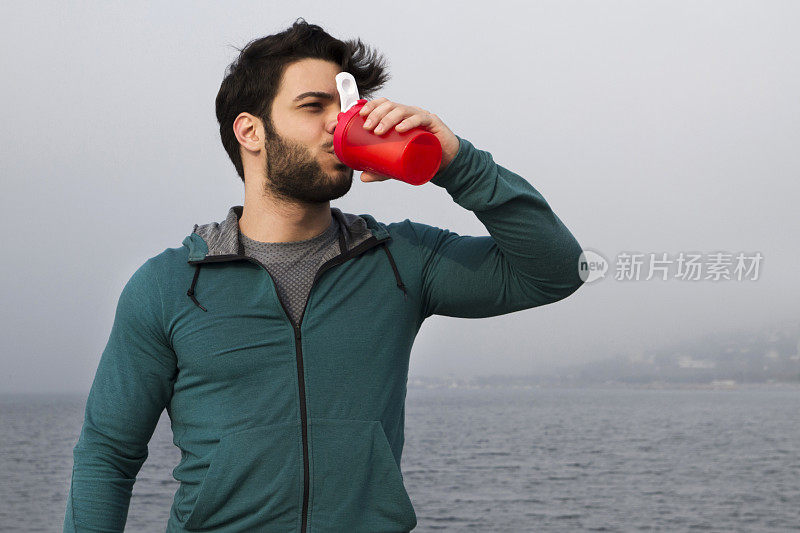 一个雾天，一个年轻人在户外锻炼后喝他的蛋白质奶昔