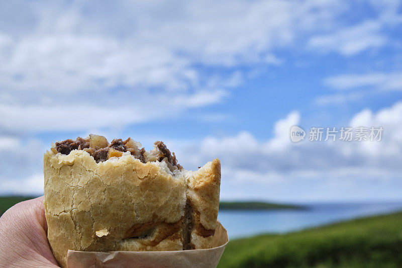 6月一个阳光明媚的日子，手里拿着吃了一半的康沃尔馅饼，俯瞰康沃尔纽基的克兰托克海滩。