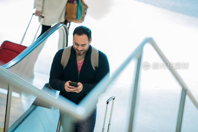 中年西班牙裔男性背着背包，在机场的自动扶梯上发短信