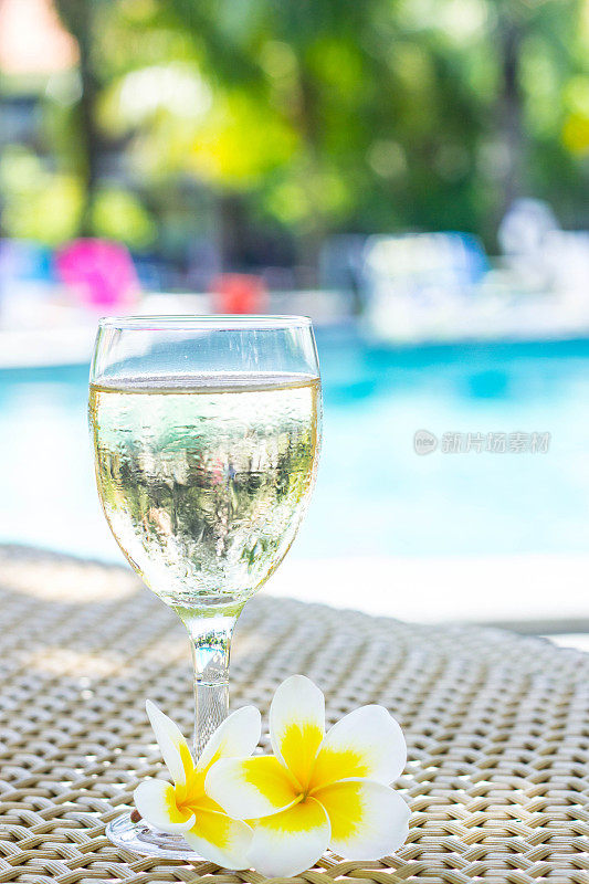 在游泳池旁边的藤桌上放着一杯白色藤蔓和热带花鸡蛋花。热带夏季度假概念。