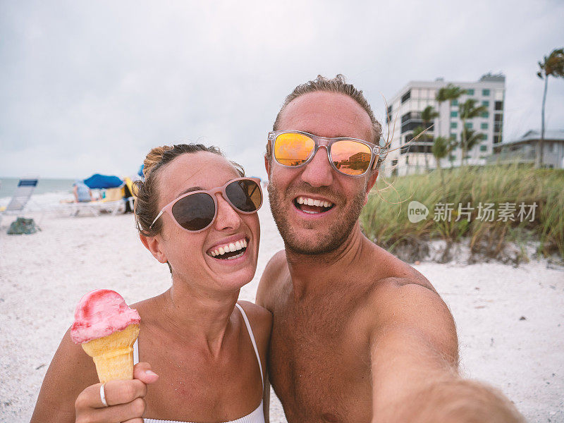 快乐的情侣在夏天的海滩上吃冰淇淋，并拍下自拍与朋友分享