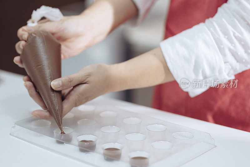 一位亚裔中国女厨师在家里准备巧克力松露，在家里的厨房里浇铸巧克力