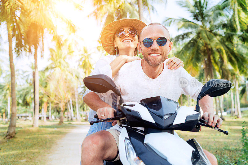 Ð一对旅行者在棕榈树下骑摩托车。旅游、度假和交通的概念形象