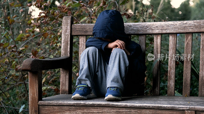 哭泣的小男孩坐在长凳上捂着脸