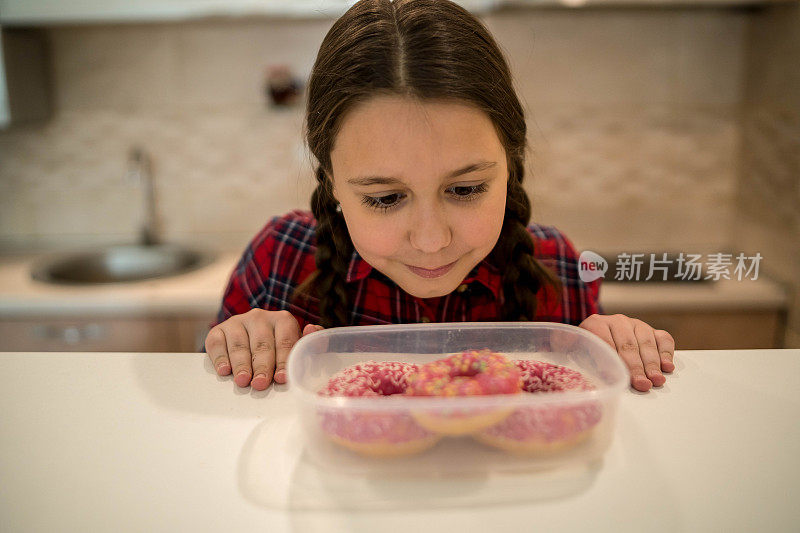 对孩子的饮食。悲伤和不快乐的孩子触及甜甜圈。孩子们的美味食物。孩子在看甜甜圈。垃圾食品上瘾。