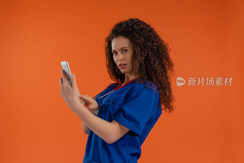 年轻女医生用智能手机盯着摄像头，橙色背景