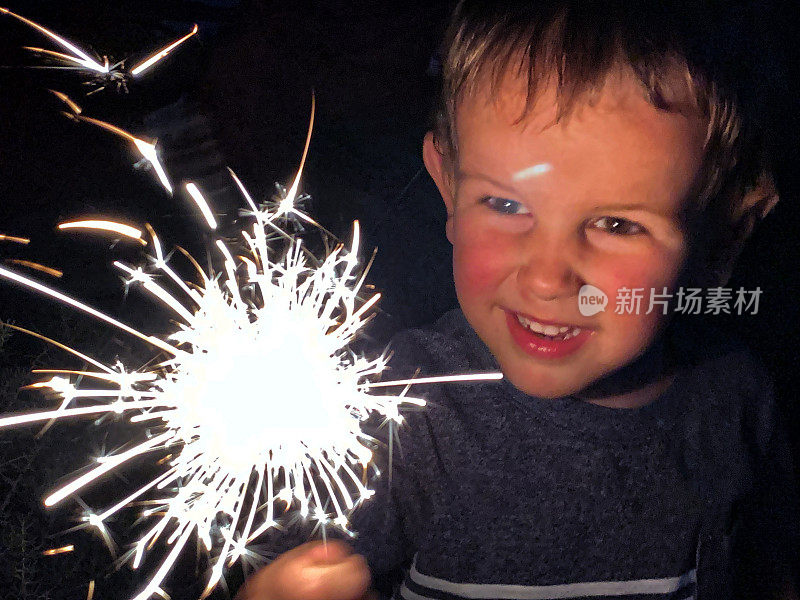 一个可爱的，四岁的白人男孩微笑着看着明亮的烟花在7月4日