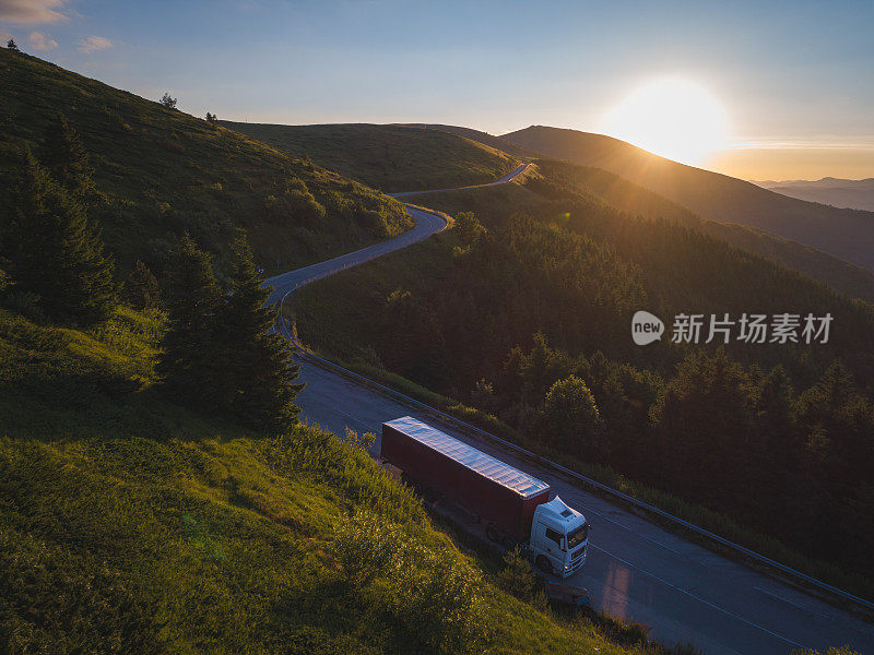 夕阳西下，快递公司载着货物行驶在蜿蜒的山路上