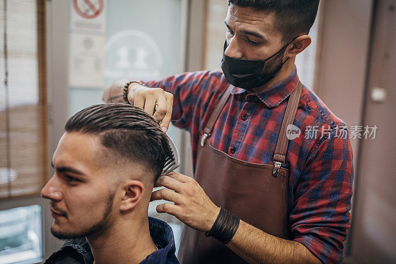 一名男子在理发店接受男理发师的理发