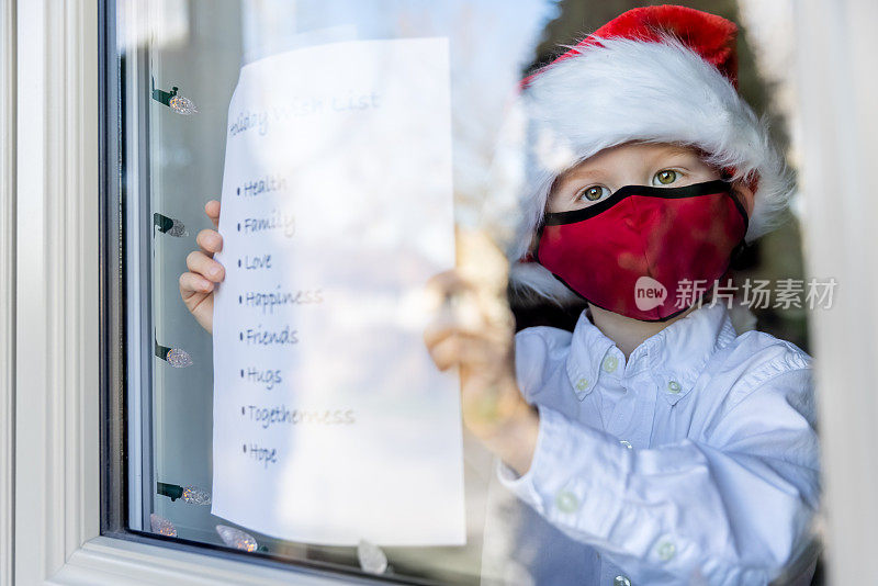 2019冠状病毒病大流行期间，一名小男孩在自家窗户上贴圣诞或节日礼物清单