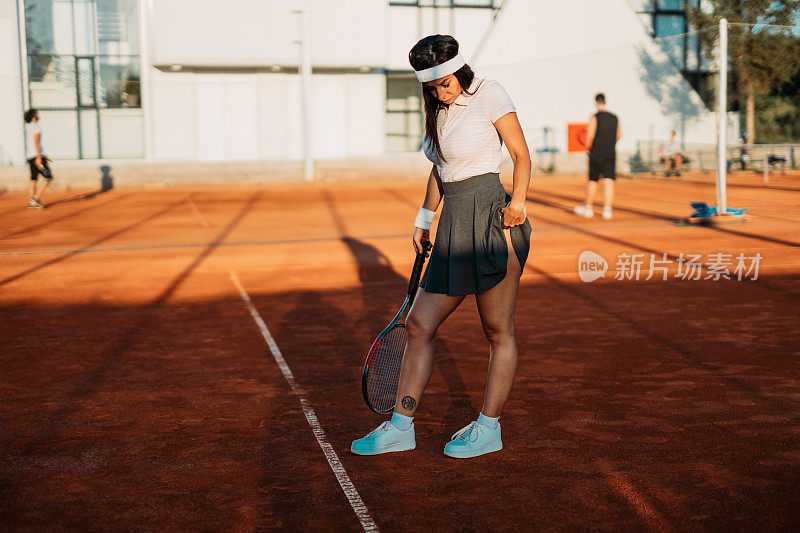 在一个阳光明媚的日子里，年轻女子网球运动员在红土场上