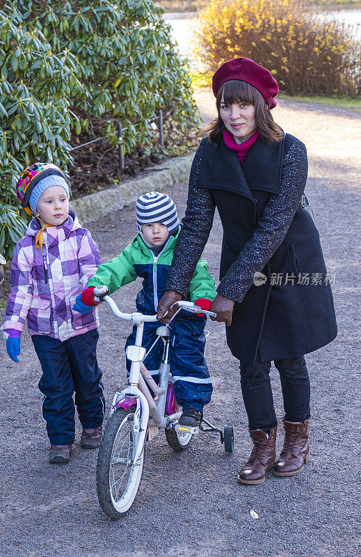 一个白人女孩带着两个小孩在城市公园里散步。秋天的阳光灿烂的日子。