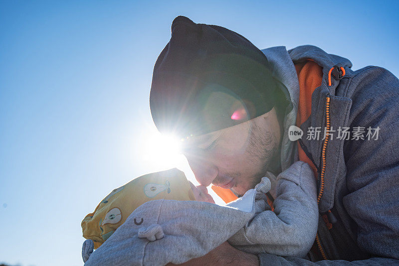 在阳光明媚的春日，父亲正在用鼻子亲吻他刚出生的男婴。