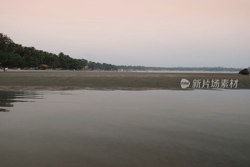 不认识的人漫步在黄昏的沙滩上，粉红色的天空日落，低潮，帕洛伦海滩，果阿，印度