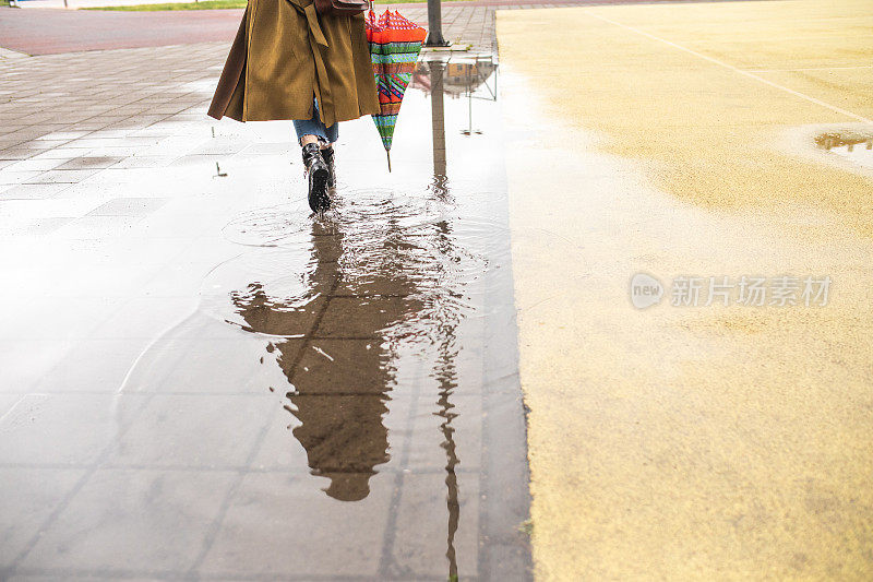 后视图，不认识的女人在大衣走过水坑在雨天在城市