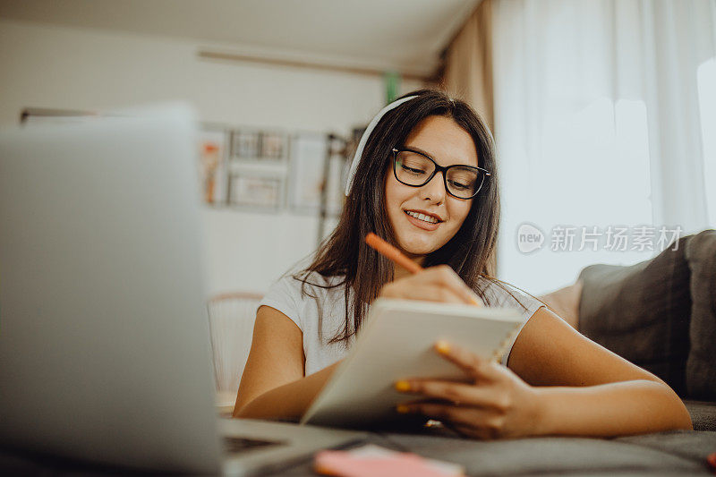 一位年轻的女学生坐在沙发上使用笔记本电脑耳机学习