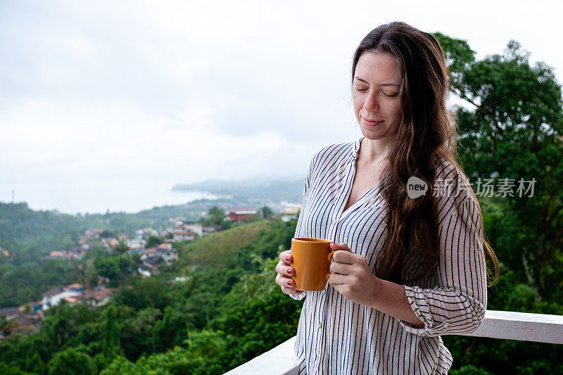 一名年轻女子在山顶上喝着茶，背景是全景