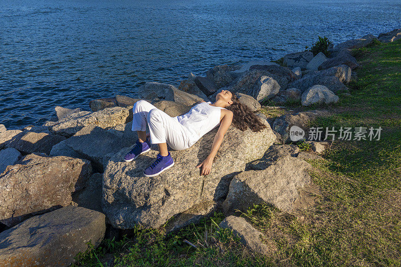 一个年轻的女人在阳光明媚的日子里躺在公园的岩石上做日光浴