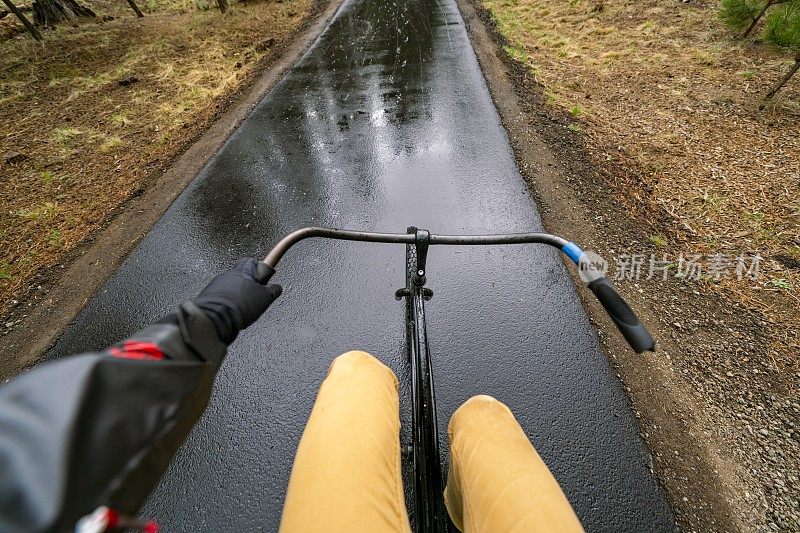 POV拍摄了一名男子在雨中骑着自行车沿着铺好的自行车道行驶