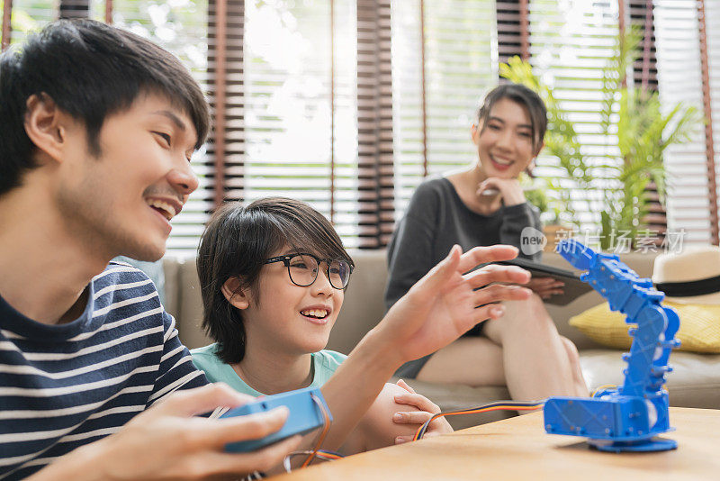 在家学习理念，亚洲男孩和父母成功控制机器人手臂在数码平板电脑和电脑键盘上，快乐的家庭在家里学习编程控制机器人