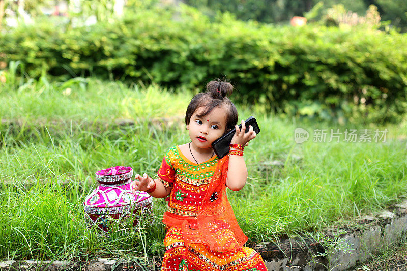 印度民族的小女孩穿着罗陀服装，在Janmashtami节上讲手机