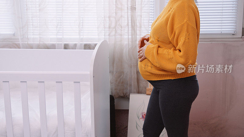 孕妇在准备婴儿床的时候抚摸着自己的肚子，幻想着她的孩子。