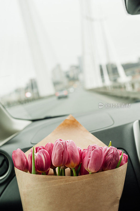 别致的一大束粉红色郁金香用牛皮纸包装在汽车内饰的道路上。花的内容，花的传递，选择性的焦点
