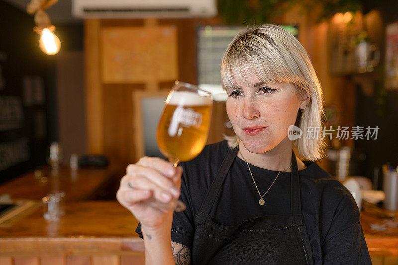 年轻的女酿酒师在品酒杯里检查啤酒的颜色