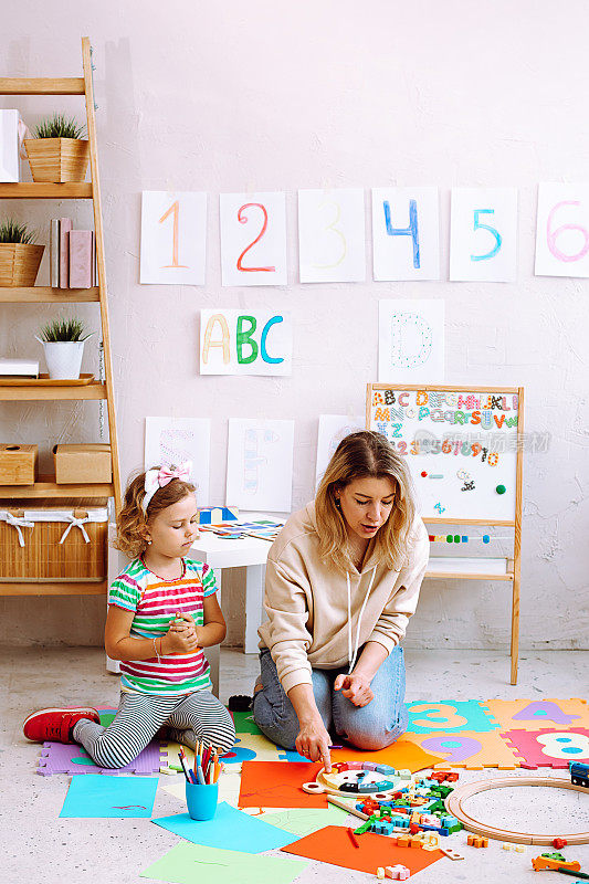画像专心的小女孩坐在年轻的女老师解释如何玩木钟在教室里。