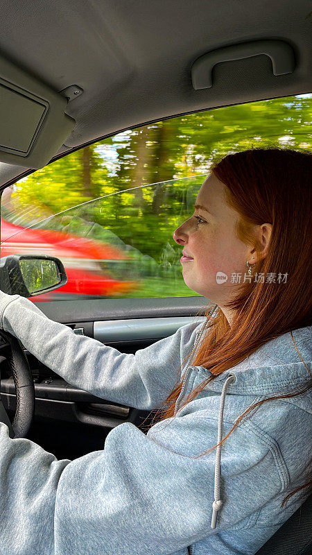 红头发的年轻女子坐在一辆车学习驾驶，集中精力驾驶右手驾驶手动车辆在英国