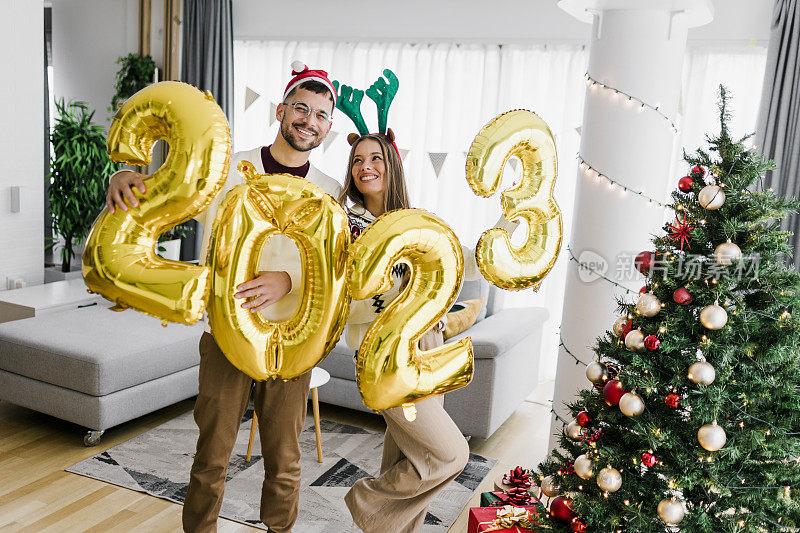 一对夫妇拿着数字2023的大气球在家里庆祝新年