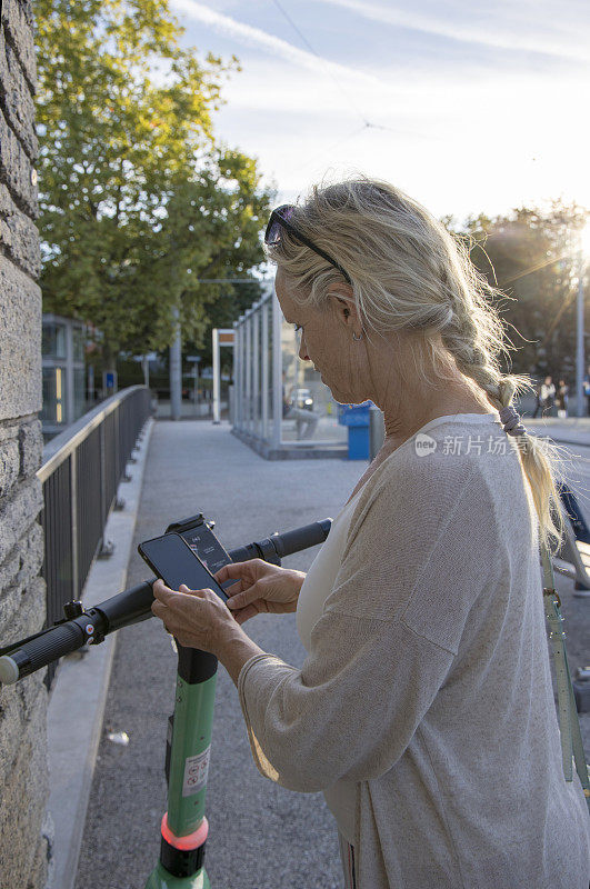 小街上，一名女子用智能手机租摩托车