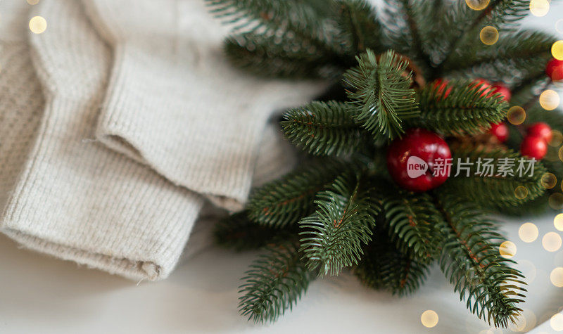 折叠针织米白色羊毛衫小松果绿色杜松枝金色灯花环在木板木桌子靠窗。舒适的冬夜。新年圣诞魔幻气氛。Scandi风格