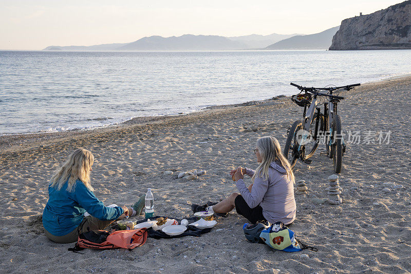 高级女自行车手在海滩上野餐
