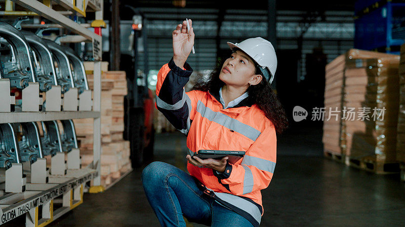 年轻的亚洲女性员工在仓库清点机械零件，并在数码平板电脑上记录数字。