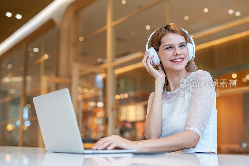 随意的商务女性，使用笔记本电脑和耳机，在带咖啡厅的工作空间进行电子学习和视频会议