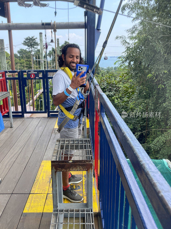 印度男子站在吊索塔甲板的安全屏障后面，背景是新加坡圣淘沙的全景林地，重点是前景