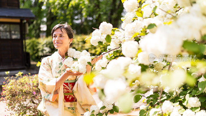 穿着和服的白人妇女站在一棵白花树旁