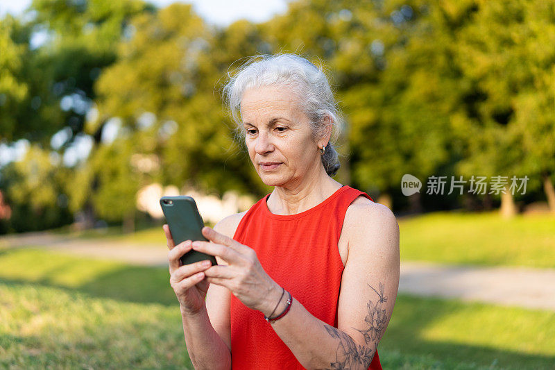 穿着红色运动服使用智能手机的资深拉丁女性。白发苍苍的老太太在公园里玩手机