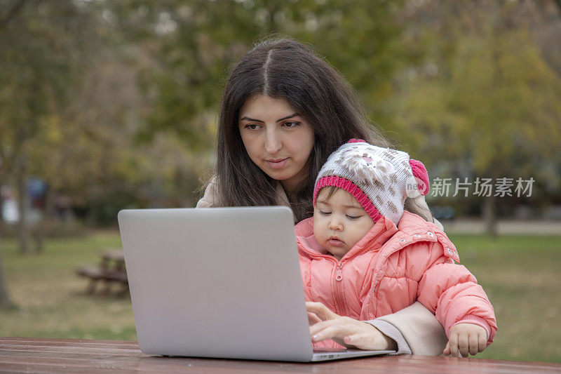 一个女人在大自然中摆弄着她的电脑，她的孩子坐在她的腿上。