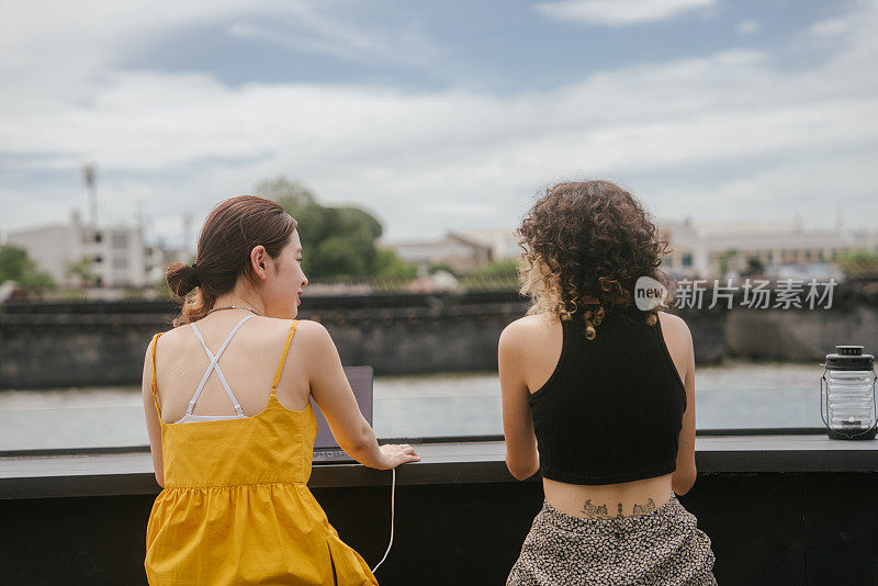 女人们坐在咖啡馆里的后景，可以看到河边的美景。度假时一起聊天放松。