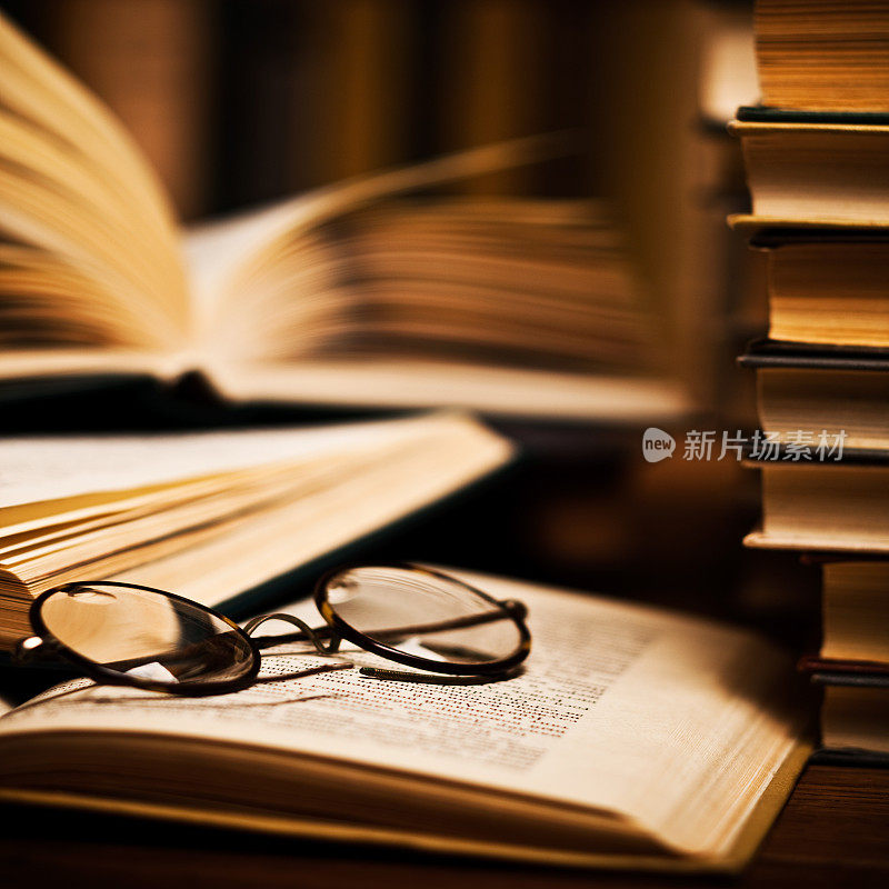 眼镜放在一本打开的书上，旁边是其他的书