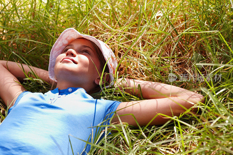 甜美的年轻女孩，双手枕在脑后，躺在草地上